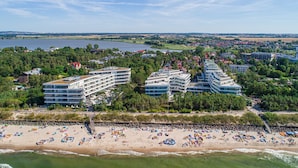 A coastal hotel with multiple floors, a beach in the foreground, and a lake in the background.