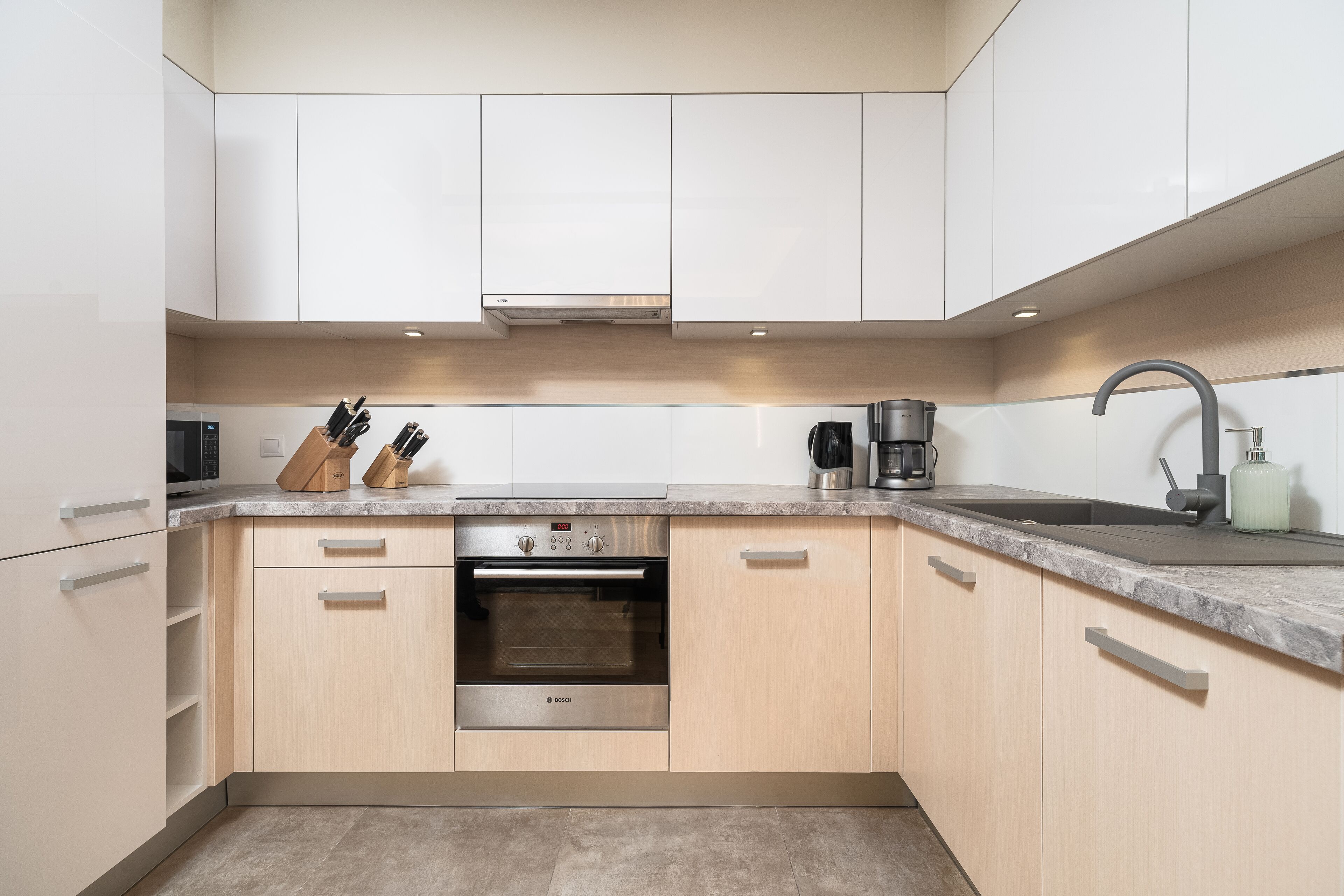 A modern kitchen with white cabinets, a Bosch oven, a sink, and a coffee maker.