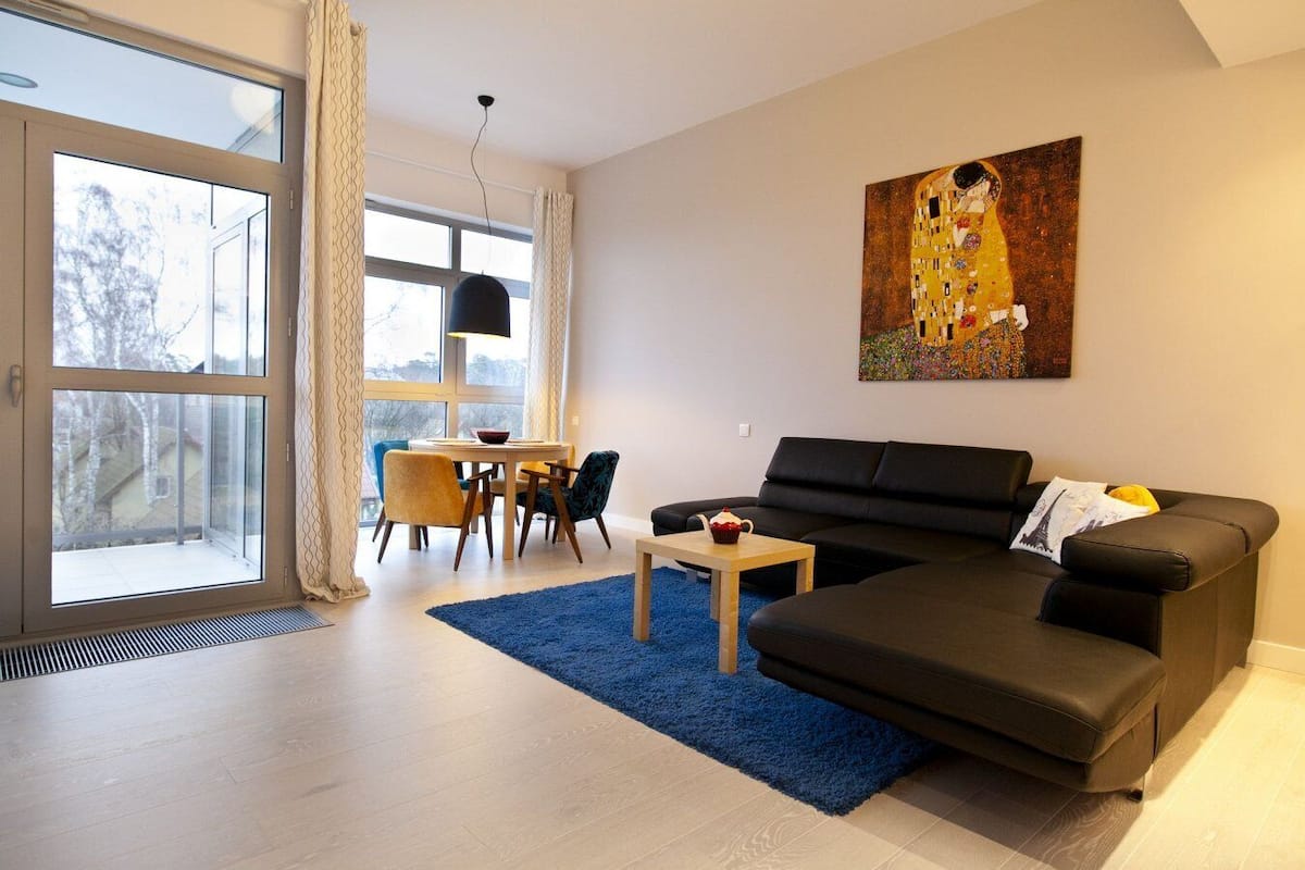 Un salon moderne avec un canapé noir, un tapis bleu et un tableau accroché au mur.
