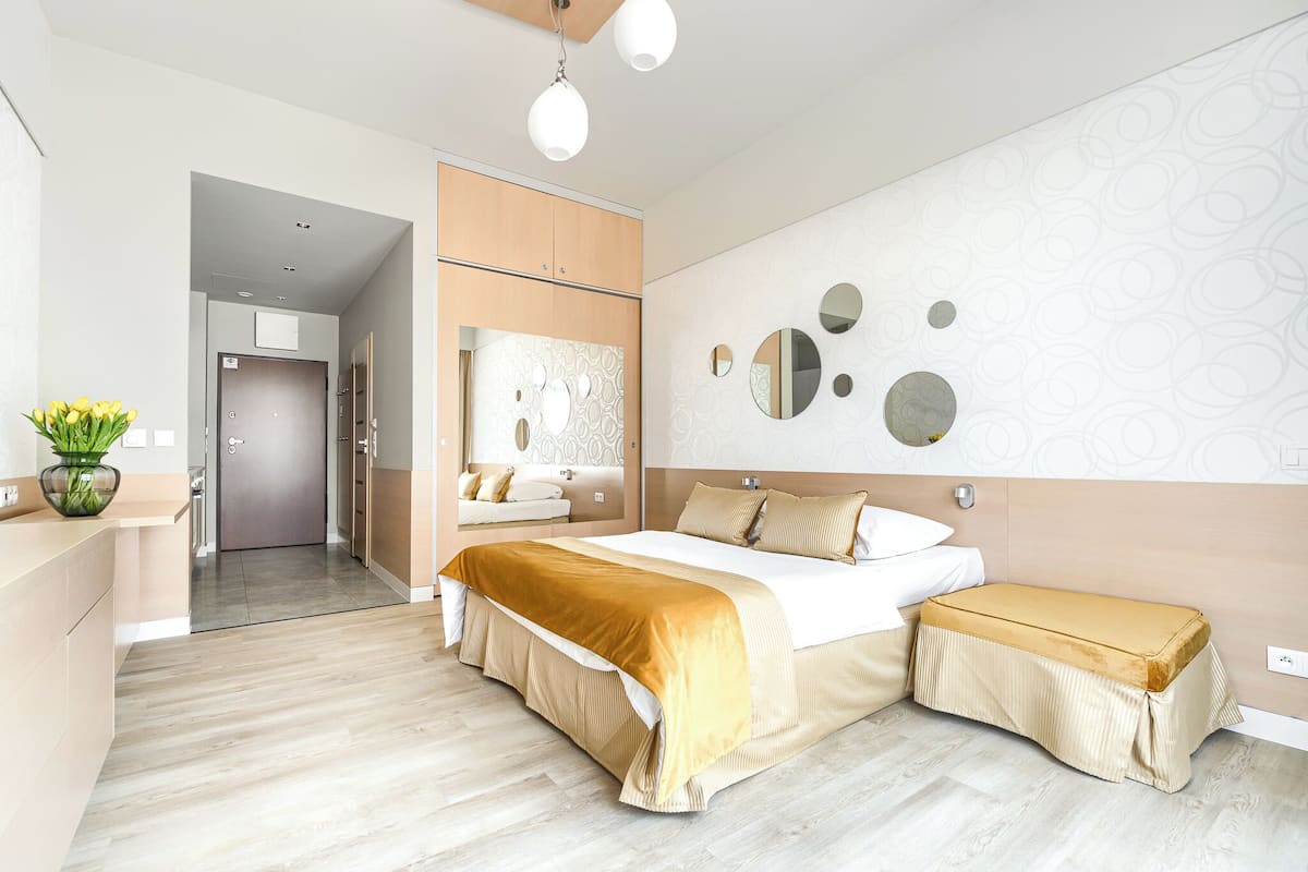 Une chambre d’hôtel moderne avec un grand lit, une table de chevet, un banc et un miroir au mur.