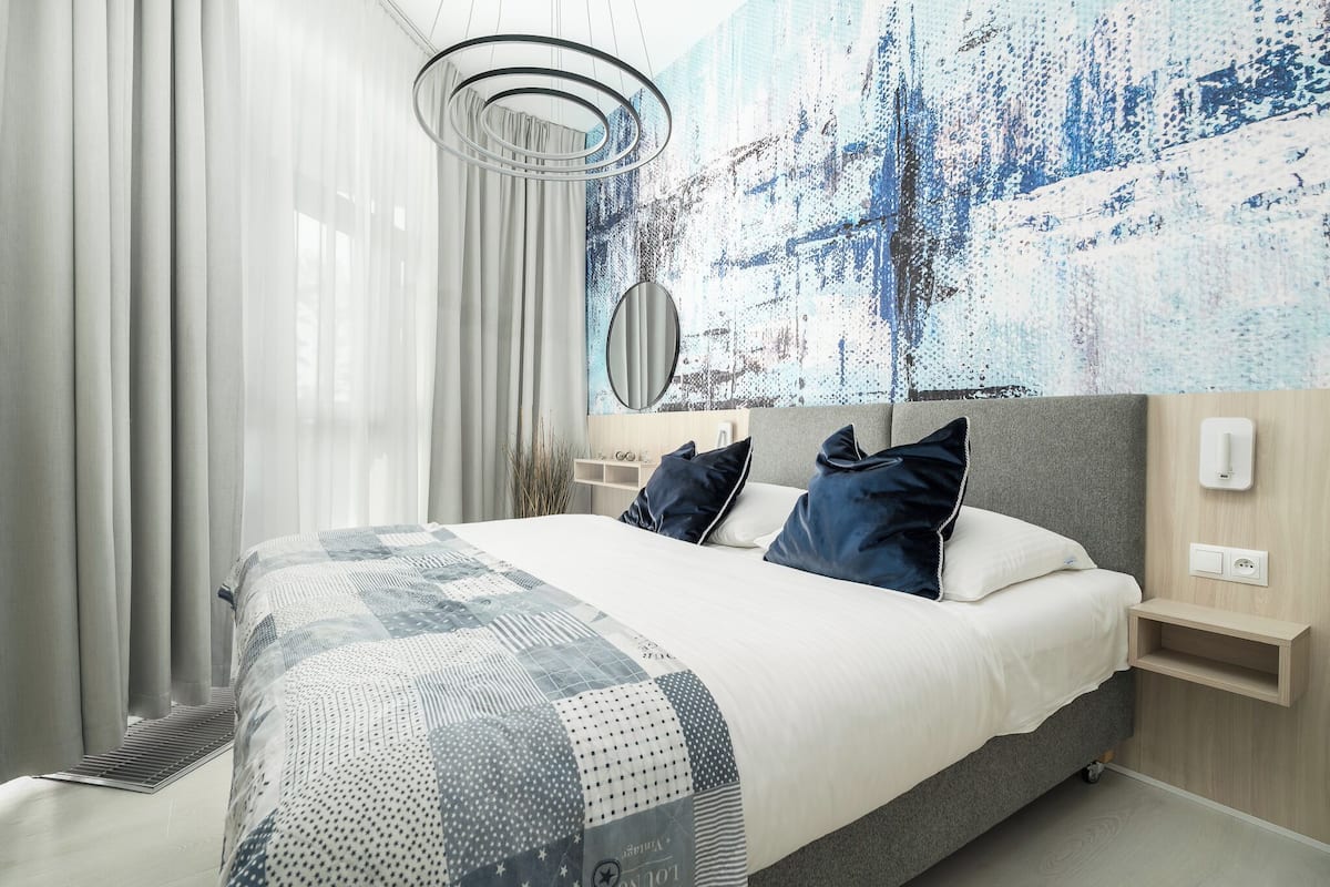 Une chambre d’hôtel moderne avec un grand lit, une table de chevet, un téléphone fixé au mur et un grand tableau abstrait.