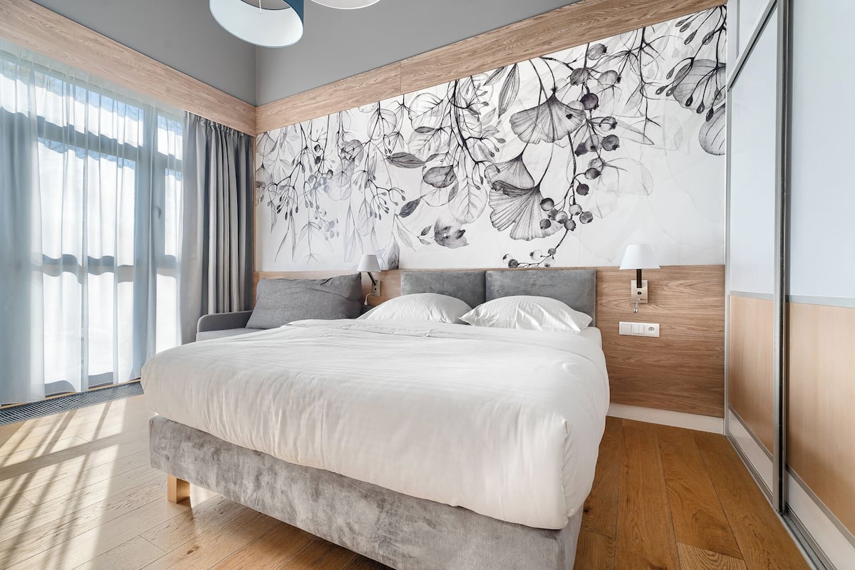 Une chambre à coucher moderne avec un grand lit, une tête de lit en bois, une fresque murale et une table de chevet avec une lampe.