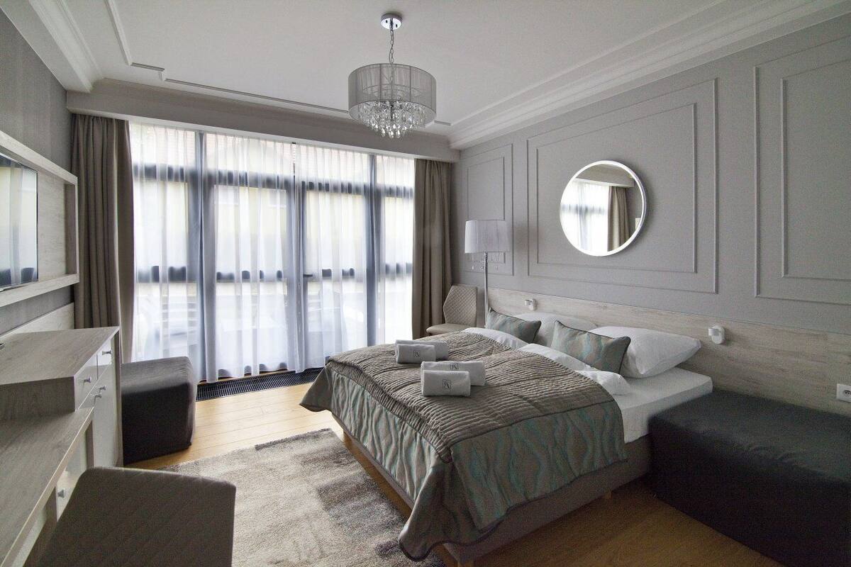 Une chambre d’hôtel moderne dotée d’un grand lit, d’un miroir rond, d’un bureau et offrant une vue sur l’extérieur grâce à de grandes fenêtres.