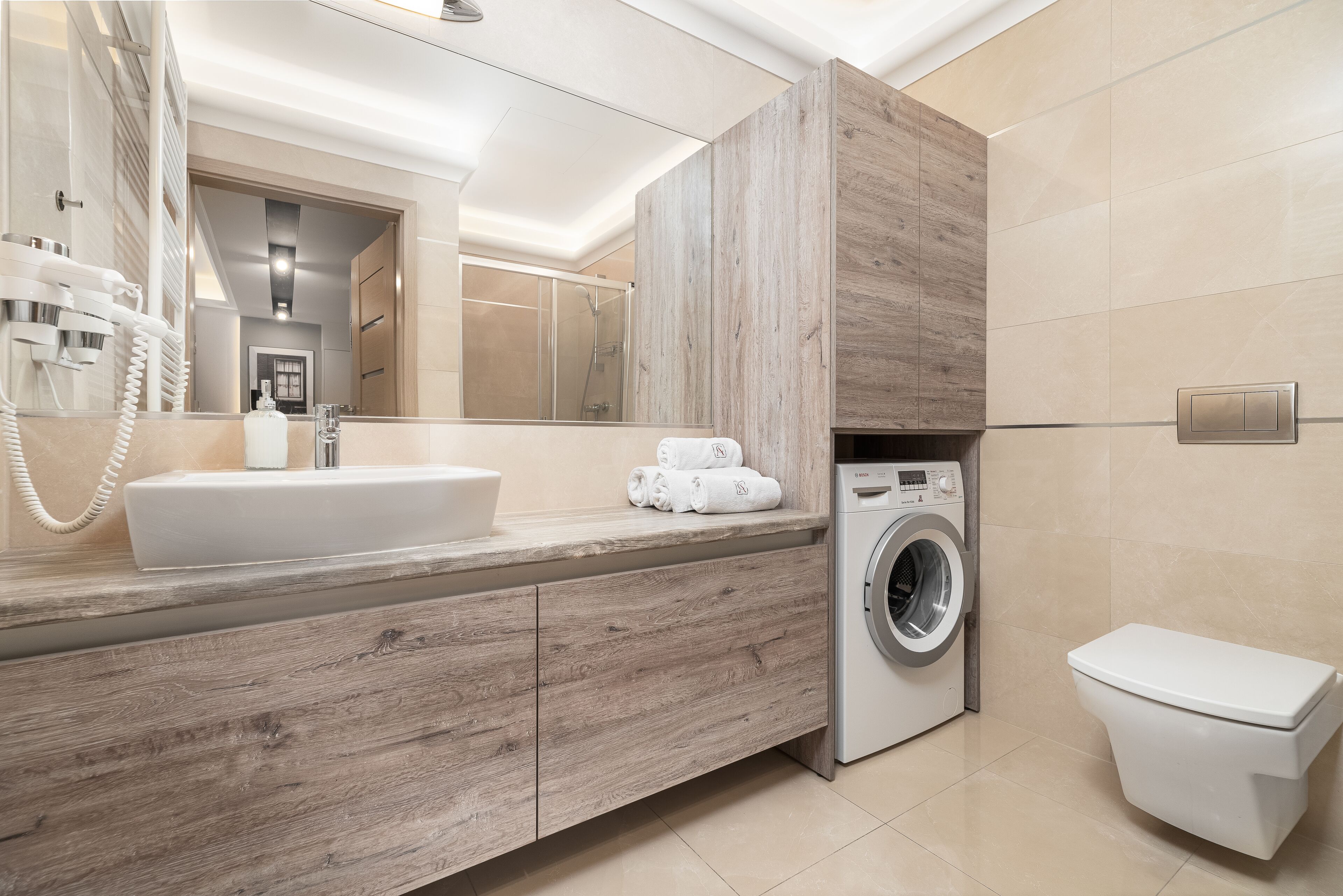 Een moderne badkamer met een houten wastafelmeubel, een ingebouwde wasmachine en een toilet.