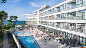 A multi-story hotel with a swimming pool, outdoor seating, and a view of the sea.