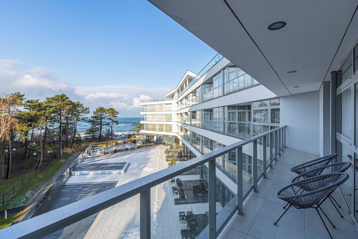 Un bâtiment moderne doté d’un balcon en verre donnant sur un paysage enneigé et un plan d’eau.