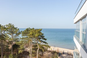 Vista costera con playa, árboles y un edificio moderno con ventanas amplias.