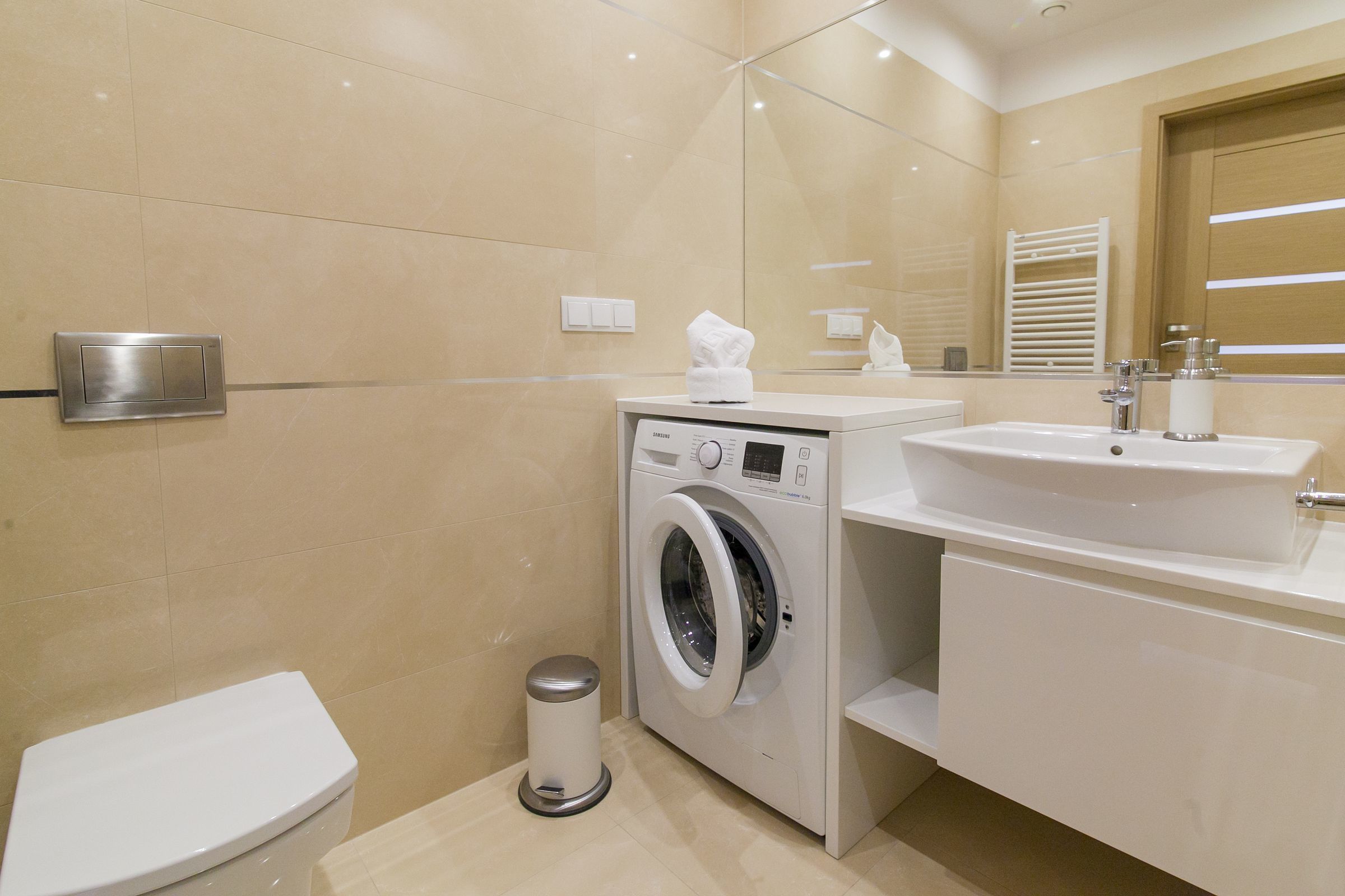 A modern bathroom with a washing machine, toilet, and sink.