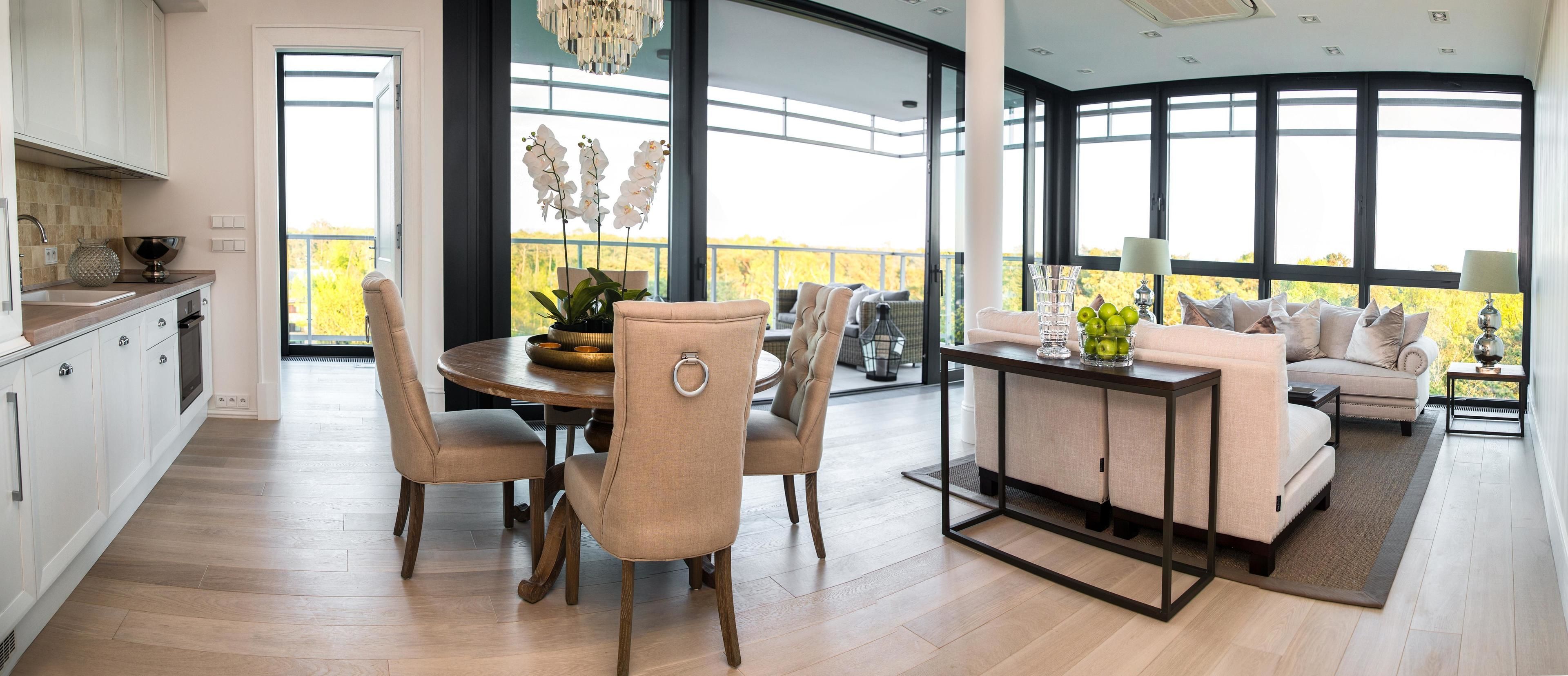 Eine moderne Küche mit weißen Schränken, ein Essbereich mit rundem Tisch und Stühlen sowie ein Balkon mit Blick auf Bäume.