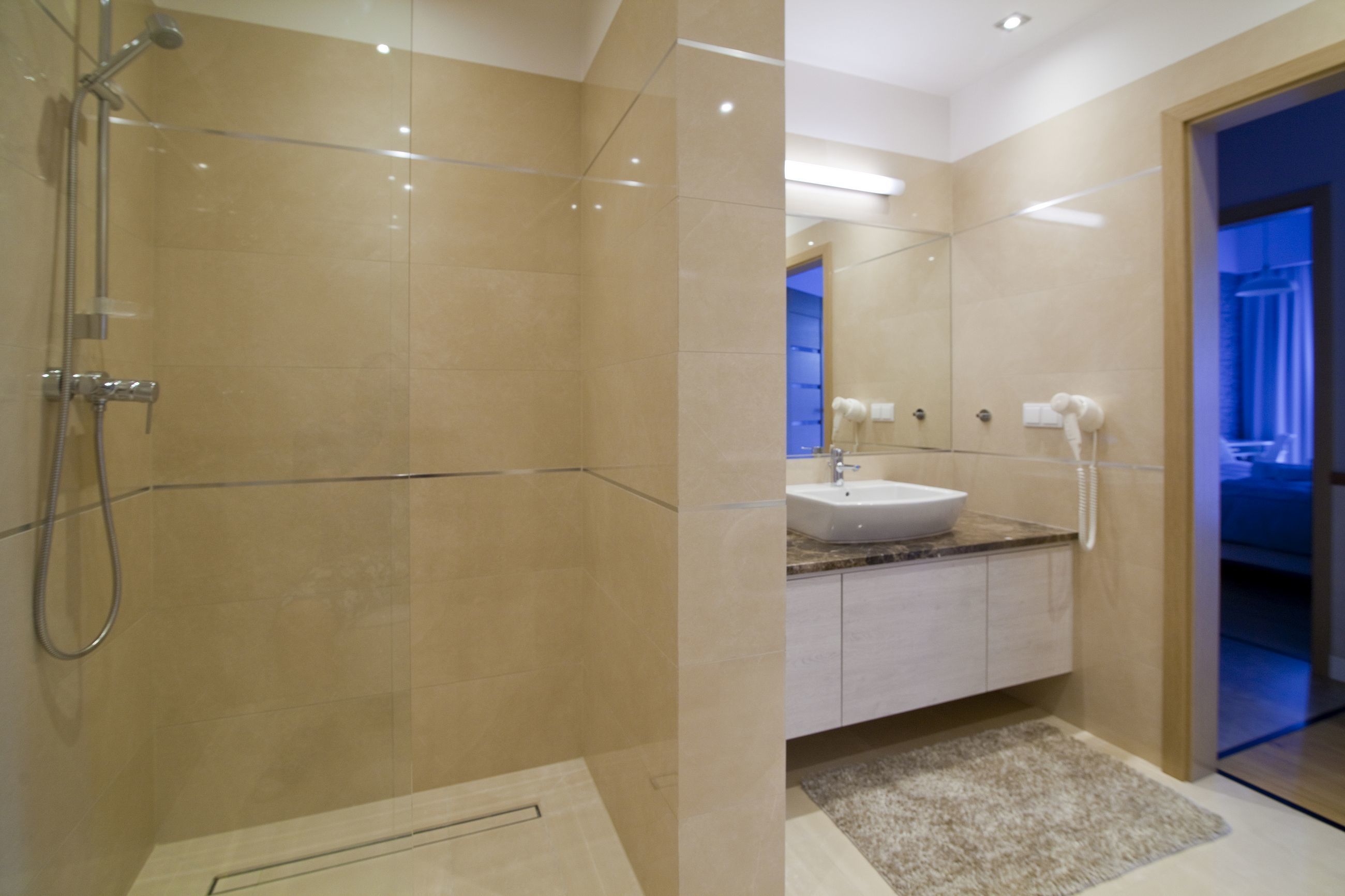 A modern bathroom with a glass shower enclosure, a white sink, and a marble countertop.