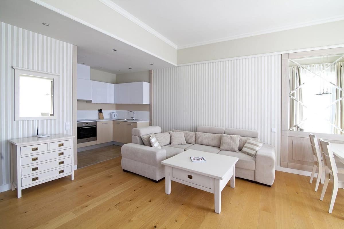 Un salon moderne avec un canapé beige, une table basse blanche et un coin repas comprenant une table et des chaises blanches.