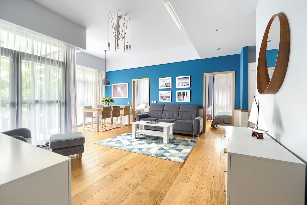 Un salon moderne avec un mur d’accent bleu, un plancher en bois, une table basse blanche, un canapé gris et un coin repas avec une table et des chaises.
