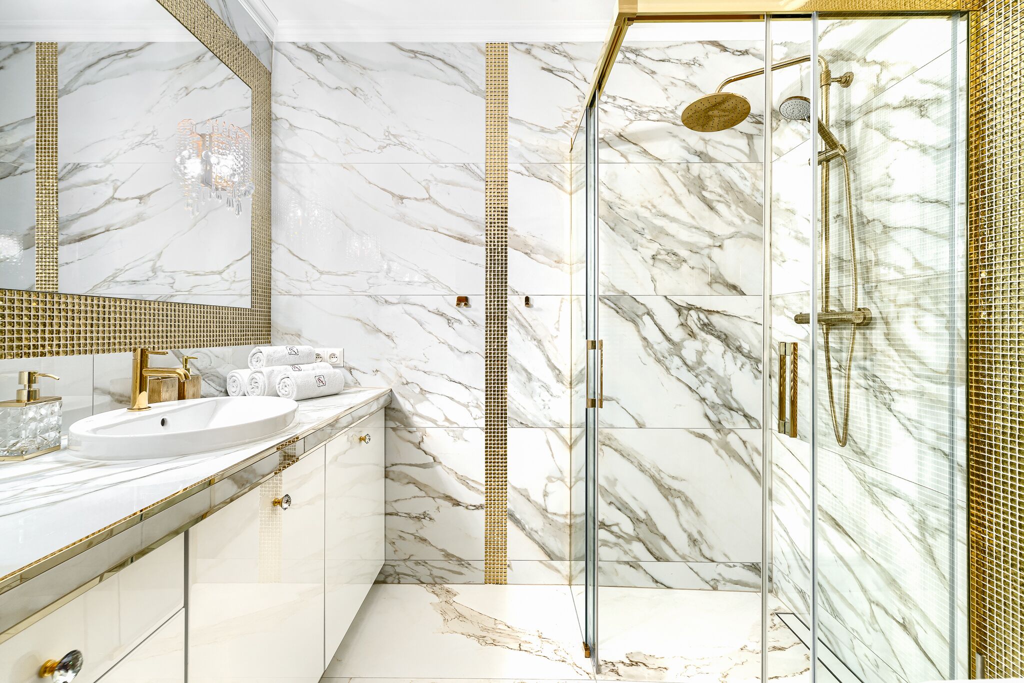 A bathroom with a marble vanity, a glass-enclosed shower, and a gold-tiled shower area.
