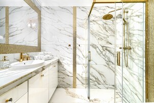 A bathroom with a marble vanity, a glass-enclosed shower, and a gold-tiled shower area.