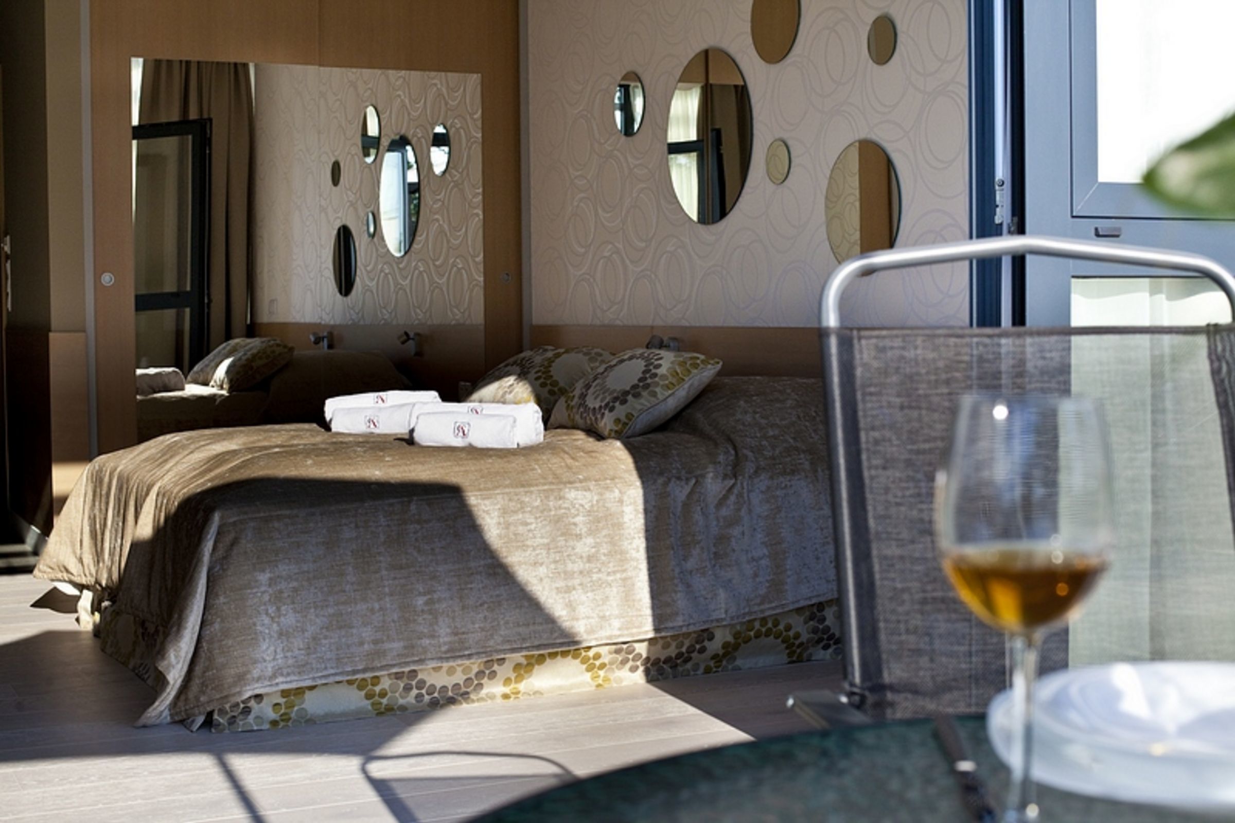 A bedroom with a bed, bedside tables, a glass of wine, and a mirror on the wall.