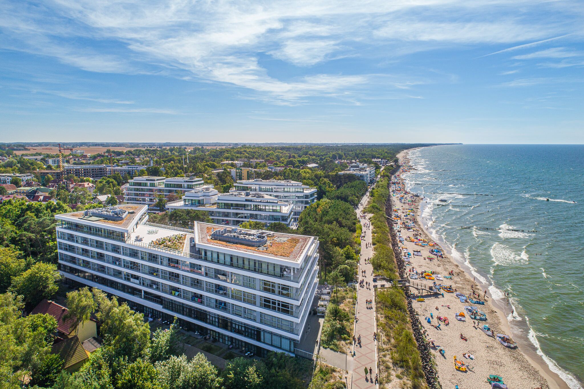 Un hotel costero con varios pisos, un paseo marítimo frente a la playa y vistas al mar.