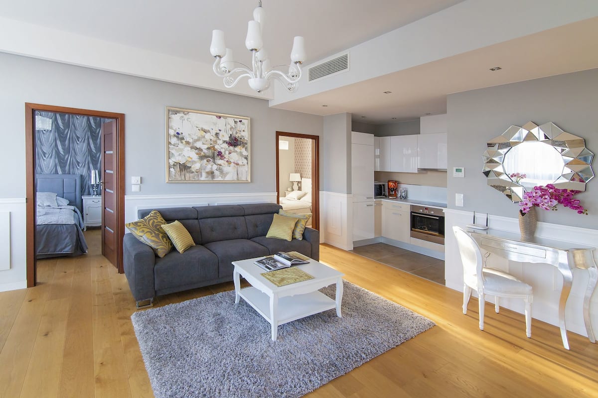 Un salon moderne avec un canapé gris, une table basse blanche et un coin cuisine doté de meubles blancs et d’une table à manger.