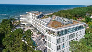 A multi-story hotel with a rooftop terrace, surrounded by greenery and overlooking the sea.