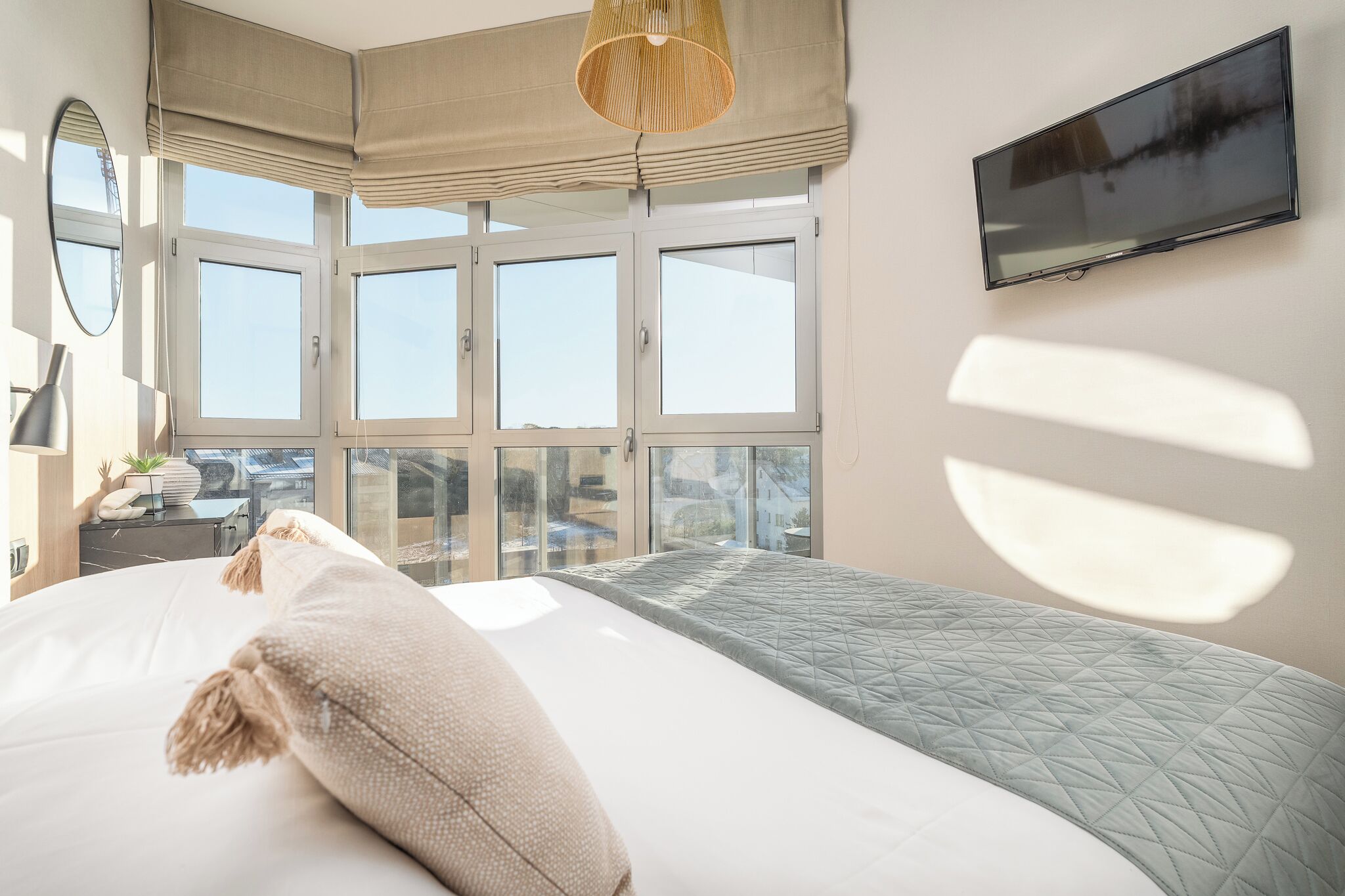 A bedroom with a large bed, a TV mounted on the wall, and a window with blinds.