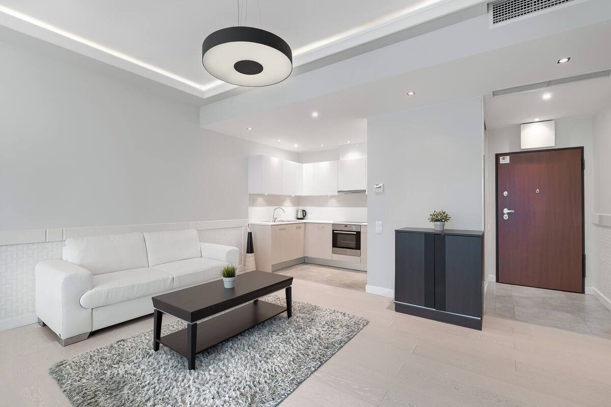 Un salon moderne avec un canapé blanc, une table basse foncée et une cuisine en arrière-plan.