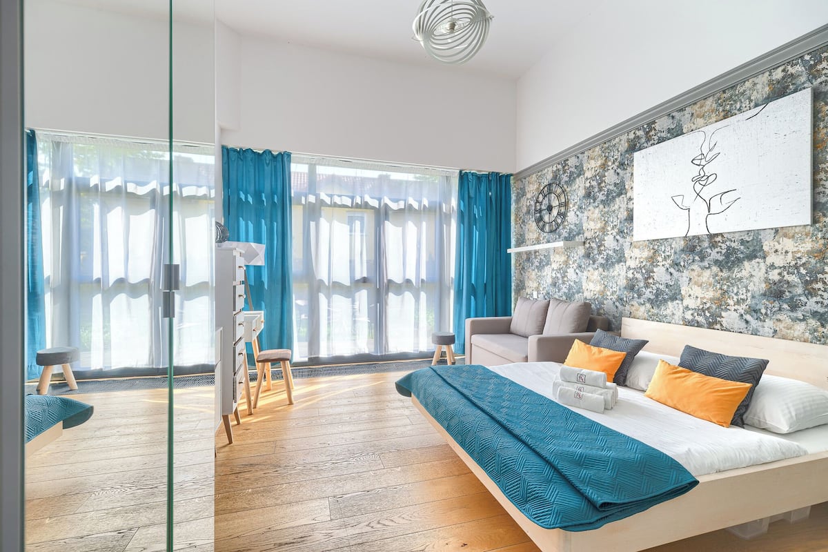 Une chambre moderne avec un grand lit, une vue sur l’extérieur et une œuvre d’art murale originale.