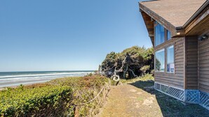 A wooden cabin with large windows overlooking a beach. - Ocean Front Home on a Sandy Beach Near Yachats! (Yachats)