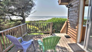 A wooden deck with two chairs, a table, and a view of the ocean. - Ocean Front Home on a Sandy Beach Near Yachats! (Yachats)