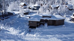 Una cabaña nevada con varias cabañas, rodeada de árboles.
