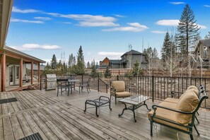 Una terraza de madera con mobiliario exterior, incluyendo una mesa, sillas y una parrilla.