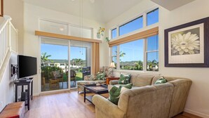 A spacious living room with a large window, a sofa, a coffee table, and a television. - Aloha Condos, Na Hale O Keauhou, Townhome D-6, Ocean View, AC (Kailua Kona)