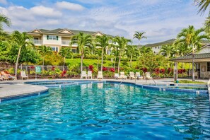 Relax by the resort's clear blue pool surrounded by lounge chairs and lush tropical plants.