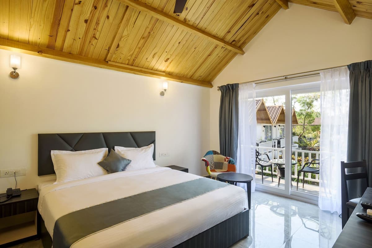 A hotel room with a large bed, a small table, a chair, and a balcony with outdoor furniture.