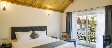 A hotel room with a bed, a nightstand, a table, and a view of the outside.