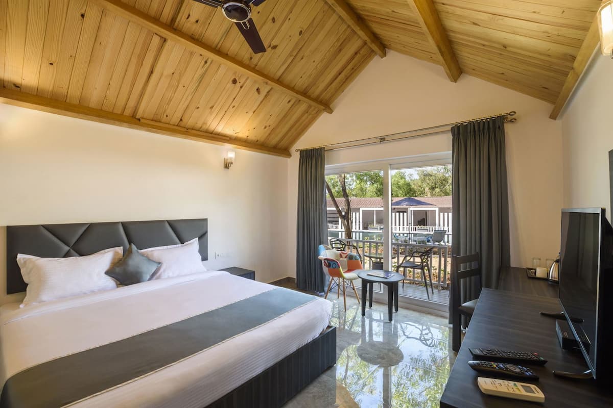 A hotel room with a bed, a TV, a desk, and a balcony with outdoor seating.