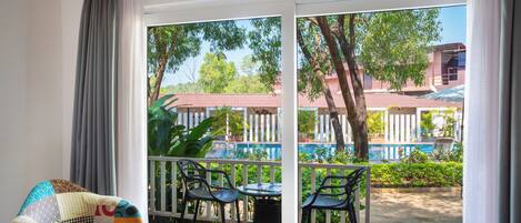 A room with a view of a pool and greenery, a patterned chair, and a small table with a cup.