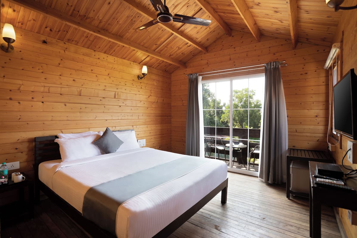 A wooden cabin bedroom with a bed, ceiling fan, and a view through a large window.
