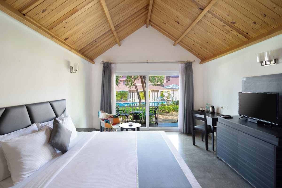 A hotel room with a large bed, a TV, a desk, and a balcony with outdoor furniture.