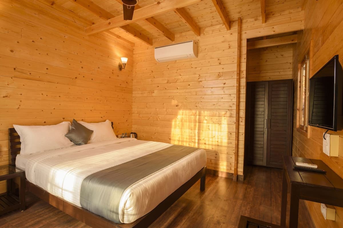 A wooden cabin room with a bed, a TV, and an air conditioning unit.
