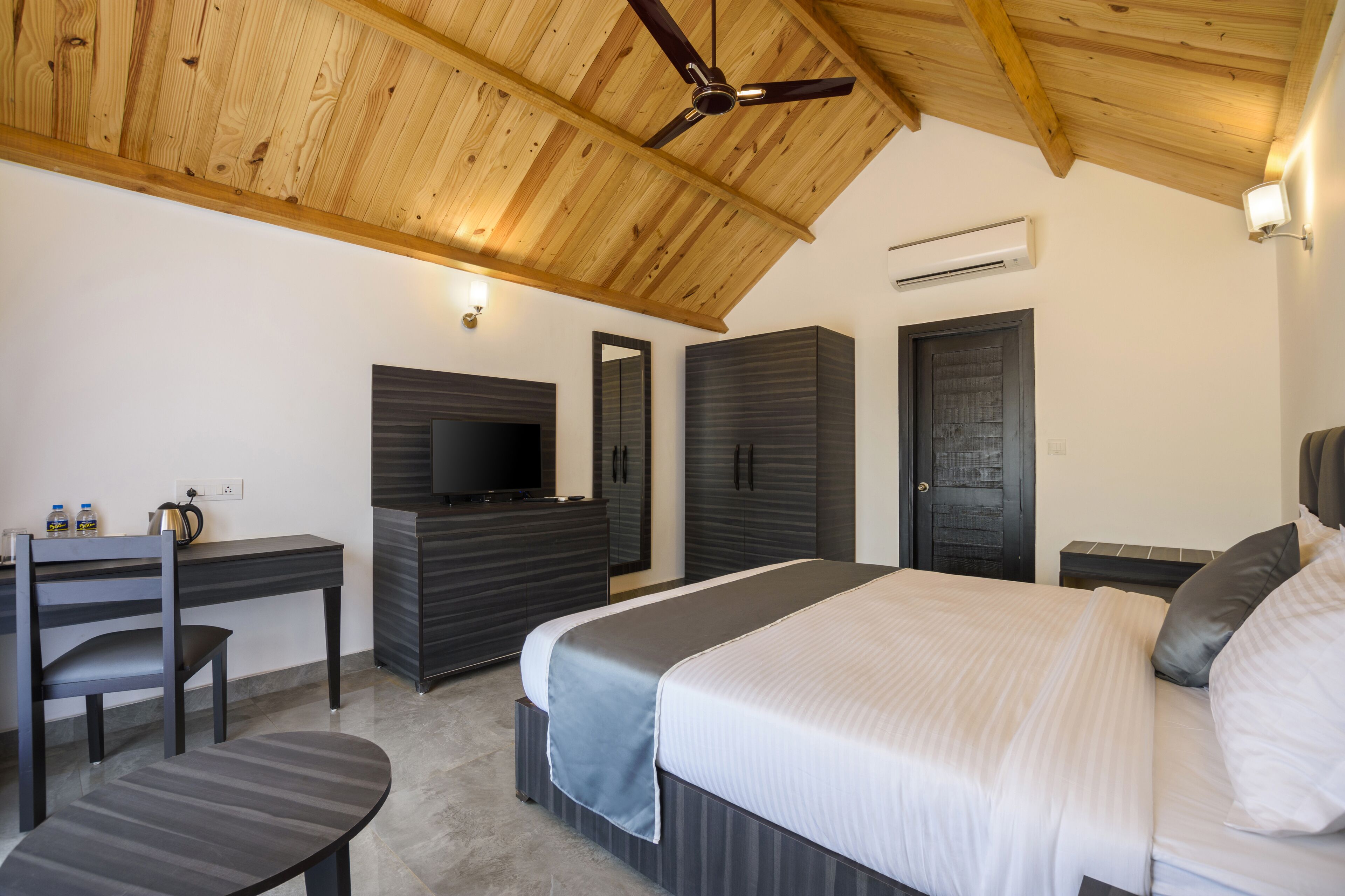 A modern bedroom with a wooden ceiling, a bed with white bedding, a desk with a chair, and a television.