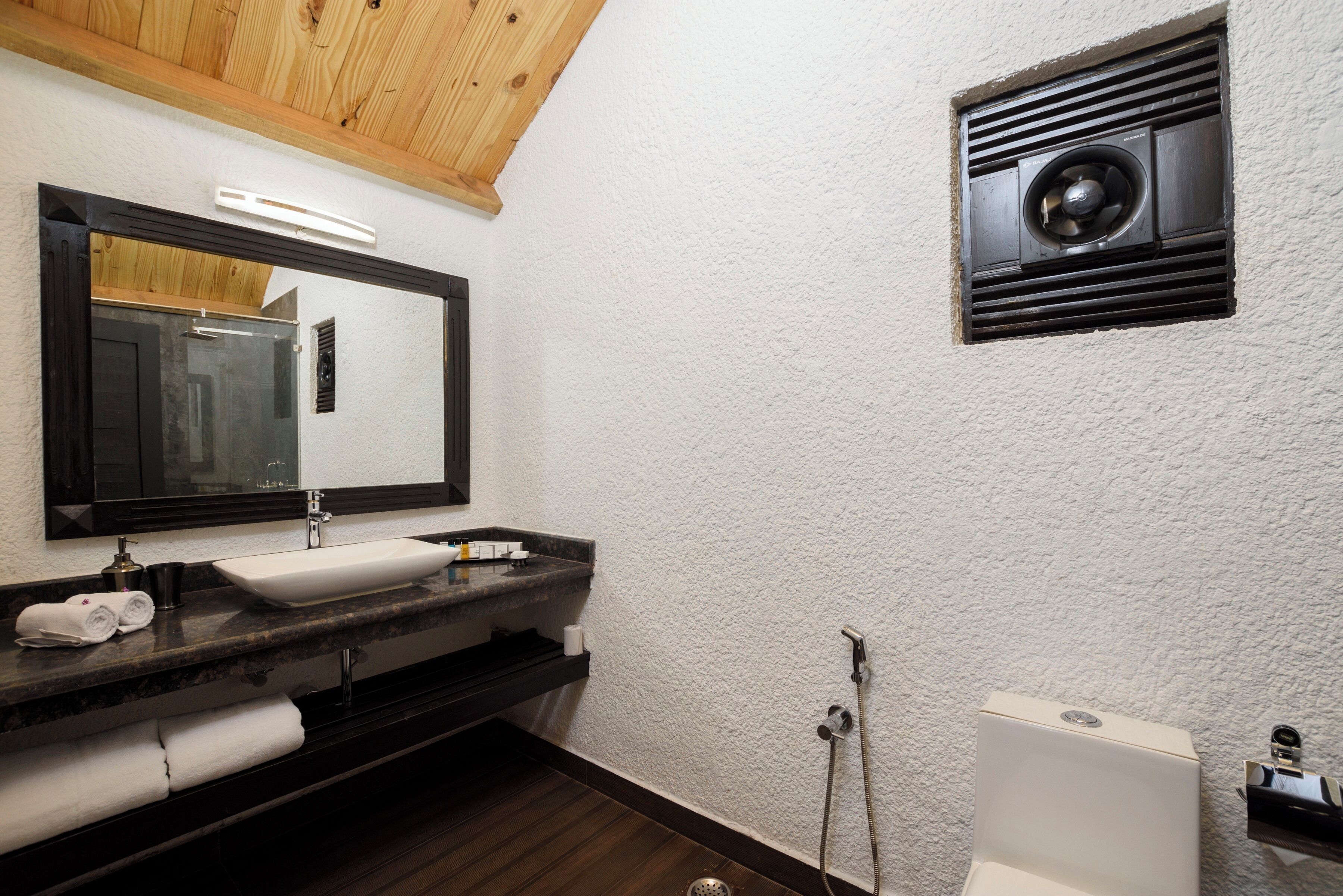 Une salle de bain avec un lavabo blanc, un plan de toilette foncé et un plafond en bois.