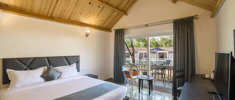 A hotel room with a large bed, a TV, a desk, and a balcony with a view of the outside.