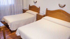 A hotel room with two single beds, wooden headboards, bedside tables, and a small table. - Pensión Residencia Buenos Aires (Vigo)