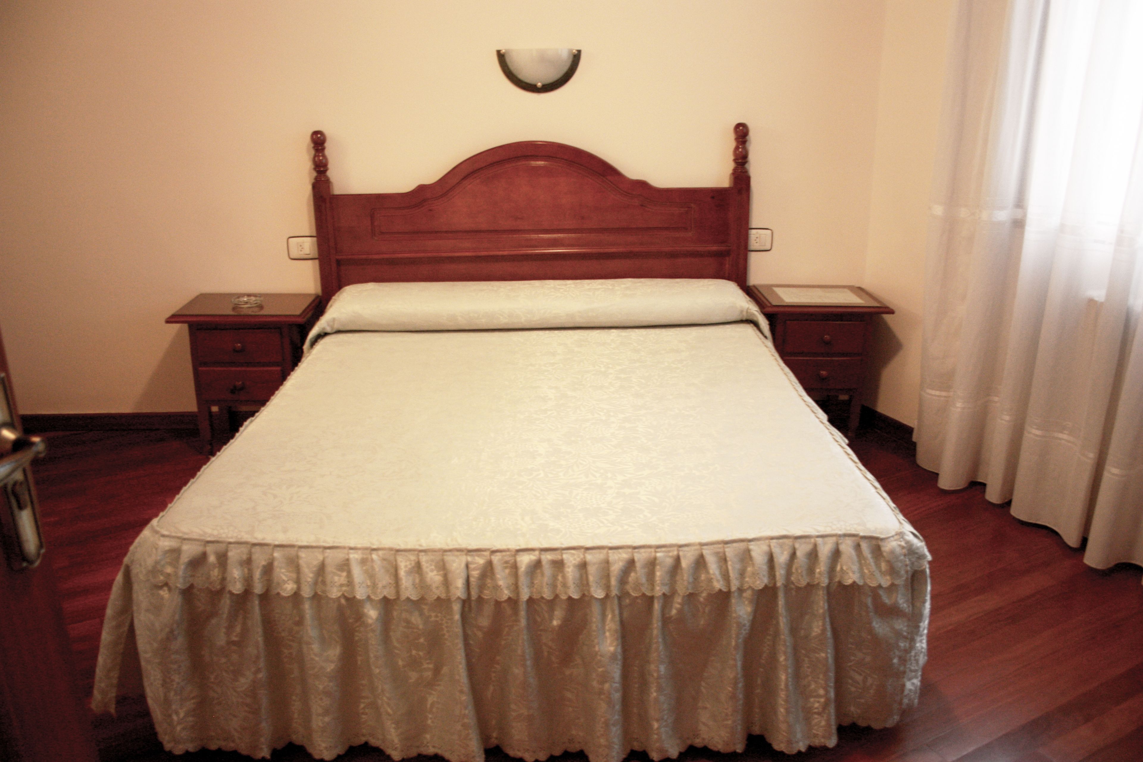 A neatly made bed with a wooden headboard, two bedside tables, and a wall-mounted light fixture.