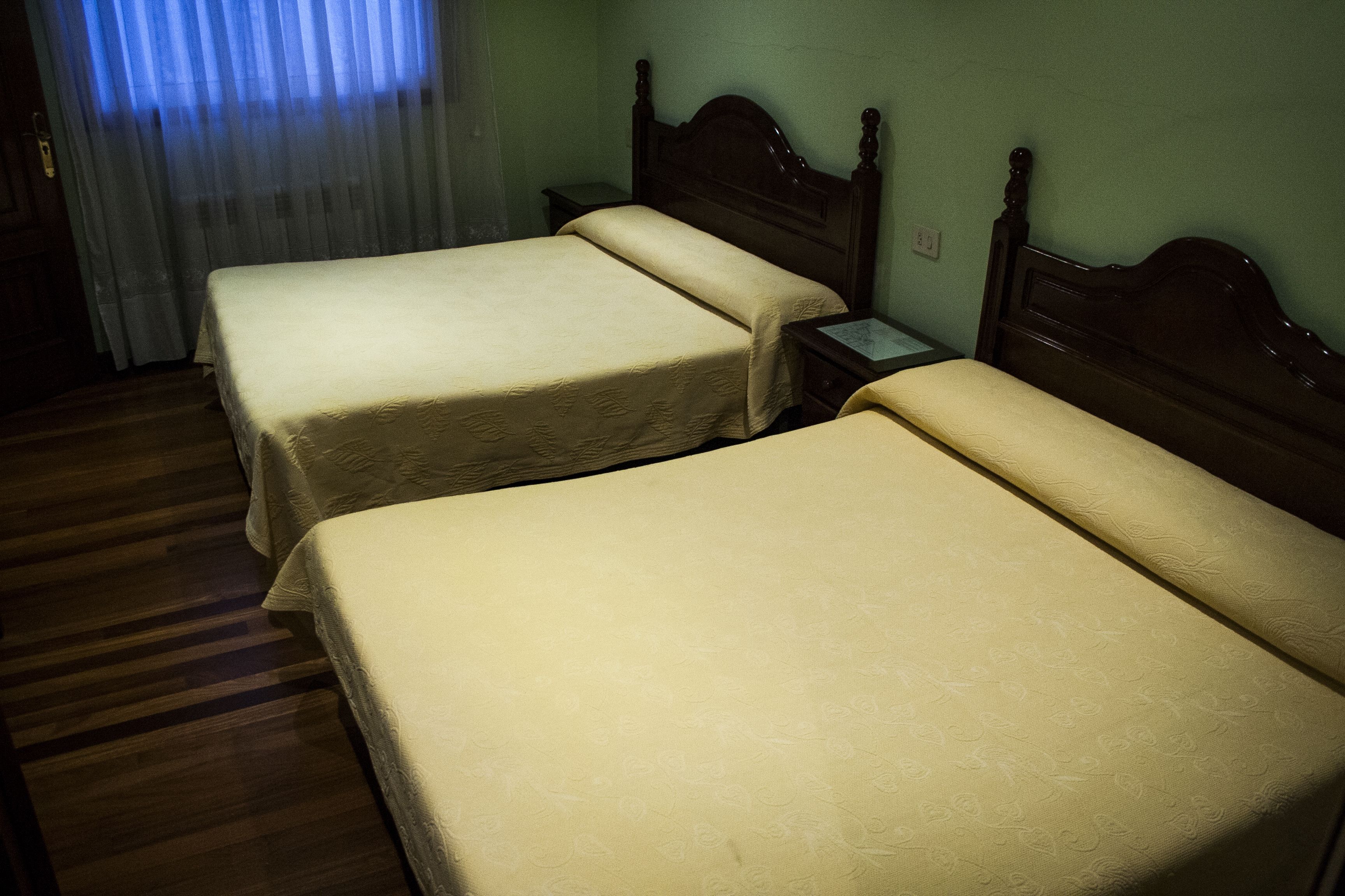 Two single beds with wooden headboards in a room with green walls and a striped carpet.