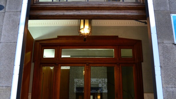 A building entrance with a wooden door, a glass panel with decorative metalwork, and a sign reading "Buenos Aires". - Pensión Residencia Buenos Aires (Vigo)
