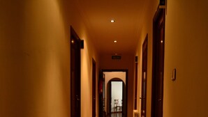 A long, narrow hallway with wooden flooring and doors on both sides, leading to a room with a chair and a table. - Pensión Residencia Buenos Aires (Vigo)