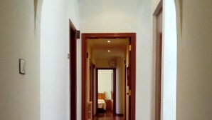 A hallway with wooden flooring and white walls, leading to a room with a bed and a nightstand. - Pensión Residencia Buenos Aires (Vigo)