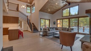 Amplia sala de estar con escaleras, una cocina y grandes ventanales que ofrecen vistas al exterior.