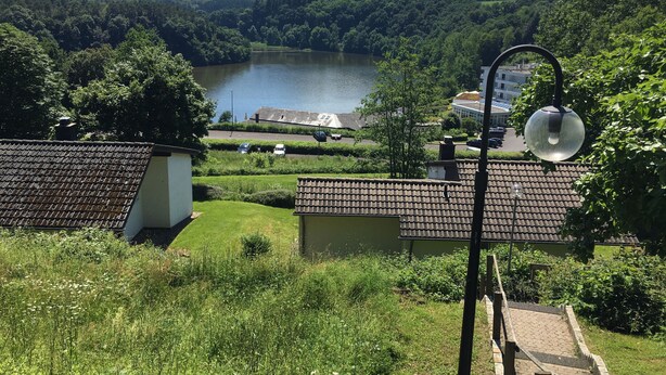 A view of a lakeside village with traditional houses, a paved path, and a lamp post. - Ferienhaus am Stausee Bitburg (Biersdorf am See)