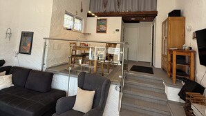 A modern living room with a sofa, armchair, and a dining area with a table and chairs. There is a staircase leading to an upper level. - Ferienhaus am Stausee Bitburg (Biersdorf am See)